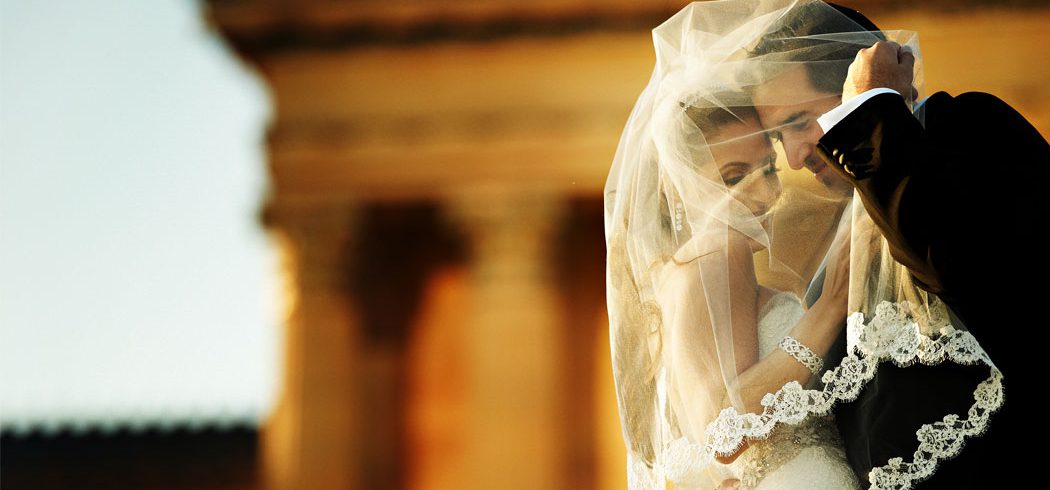 Bride and Groom embrace under veil at Philadelphia Art Museum during outside wedding portraits in Philadelphia, PA - Event Planner